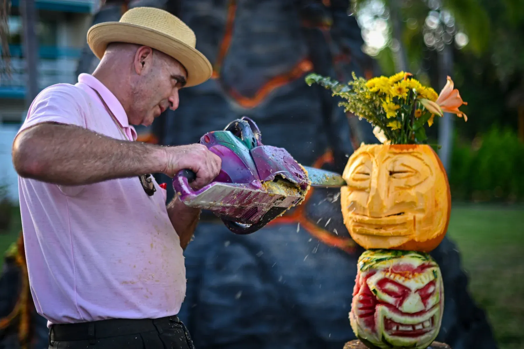 An artist chainsaw-carves tiki faces into a pumpkin and a watermelon at Tiki Fever