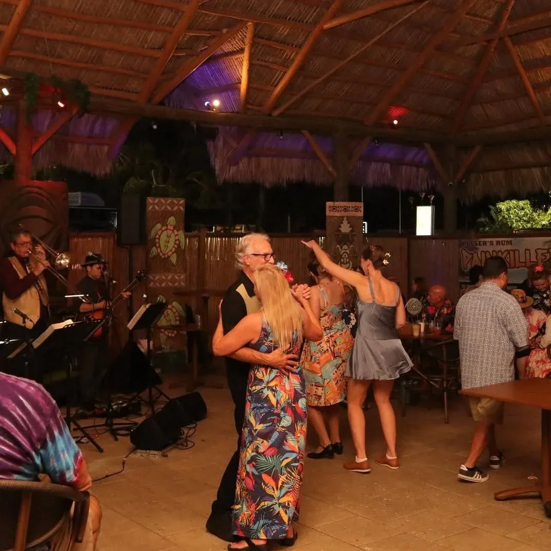 Couples dance to a live band under a thatched roof during a Tiki Fever opening-night party