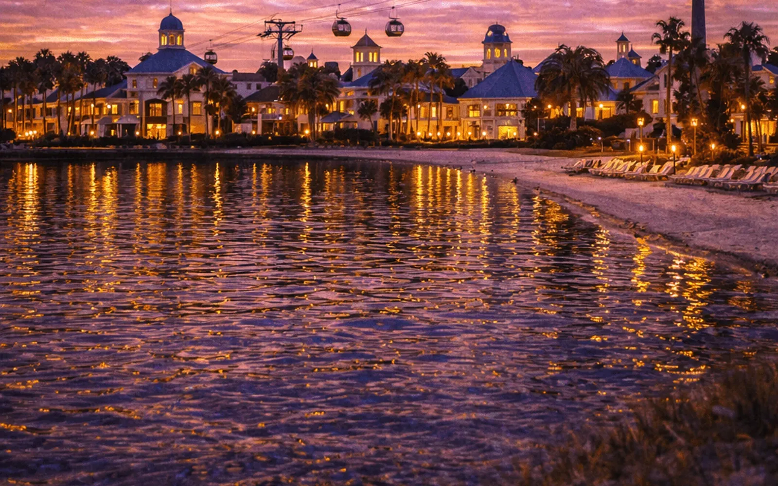 Illustrated sunset view of Disney's Caribbean Beach Resort across the water.